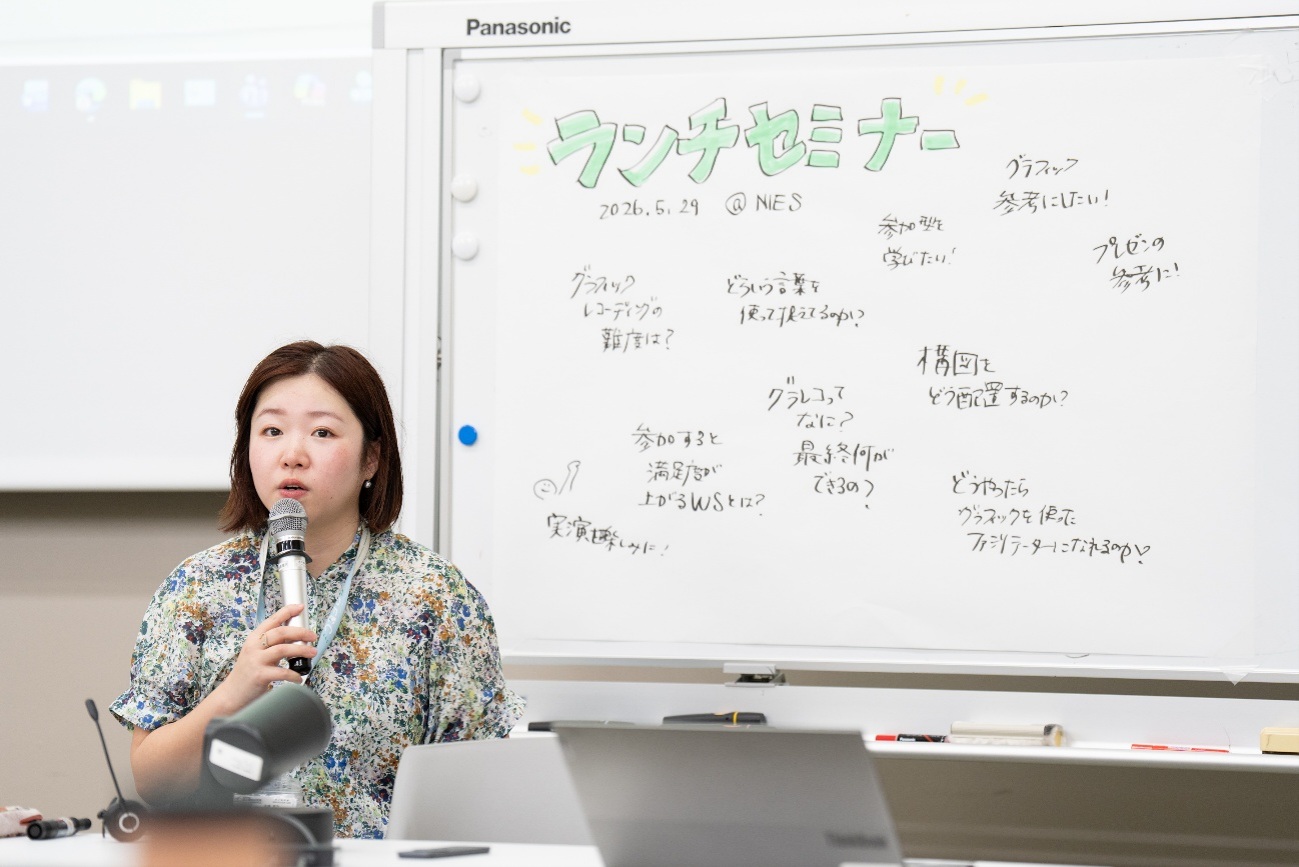 有廣さんが模造紙の前でマイクを持ち、参加者に向かって話している様子